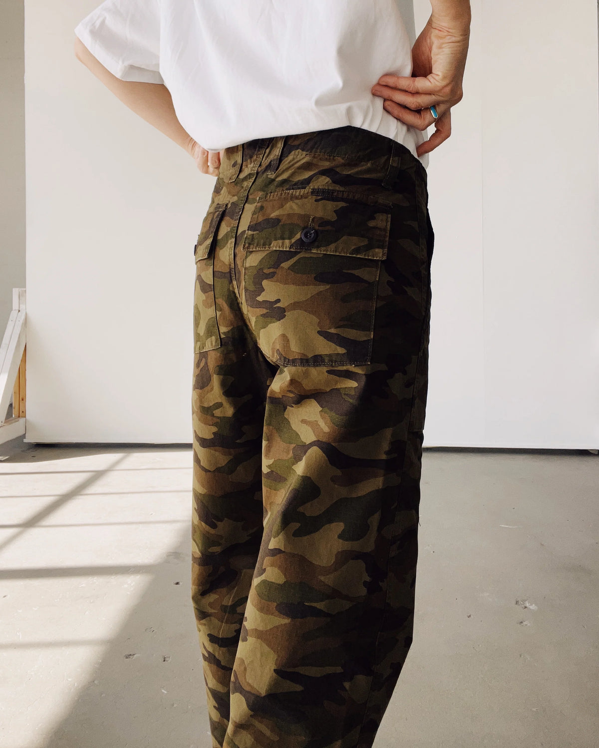A person stands indoors in sunlight, wearing Hey Gang’s The Officer Pant—a green cotton ripstop cargo pant with a loose crop fit—paired with a white T-shirt.