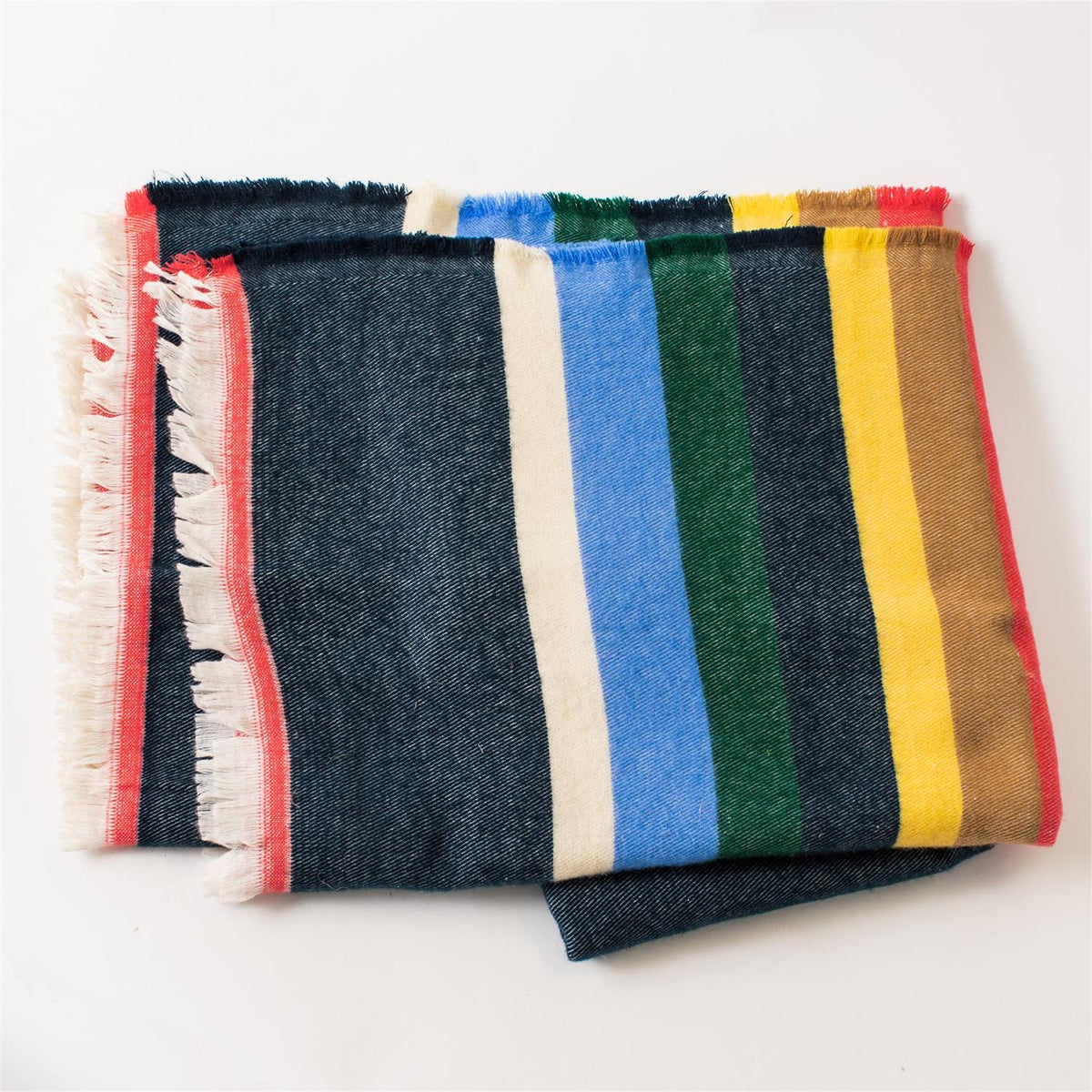 The Multicolor Cabin Stripe Throw Blanket by Faire features a dark blue base, bold vertical stripes, red border, and white fringe—ideal as a rustic accent or cabin throw—shown folded on a white background.