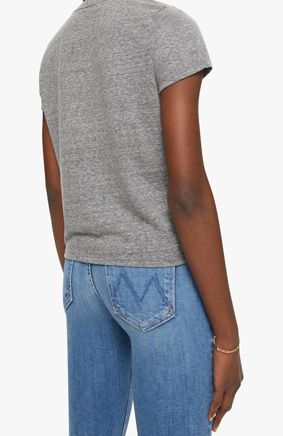 A person is shown from the back wearing Mother’s The Lil Goodie Goodie Tee in soft gray with light blue jeans, paired casually with a thin gold bracelet on their relaxed left arm.