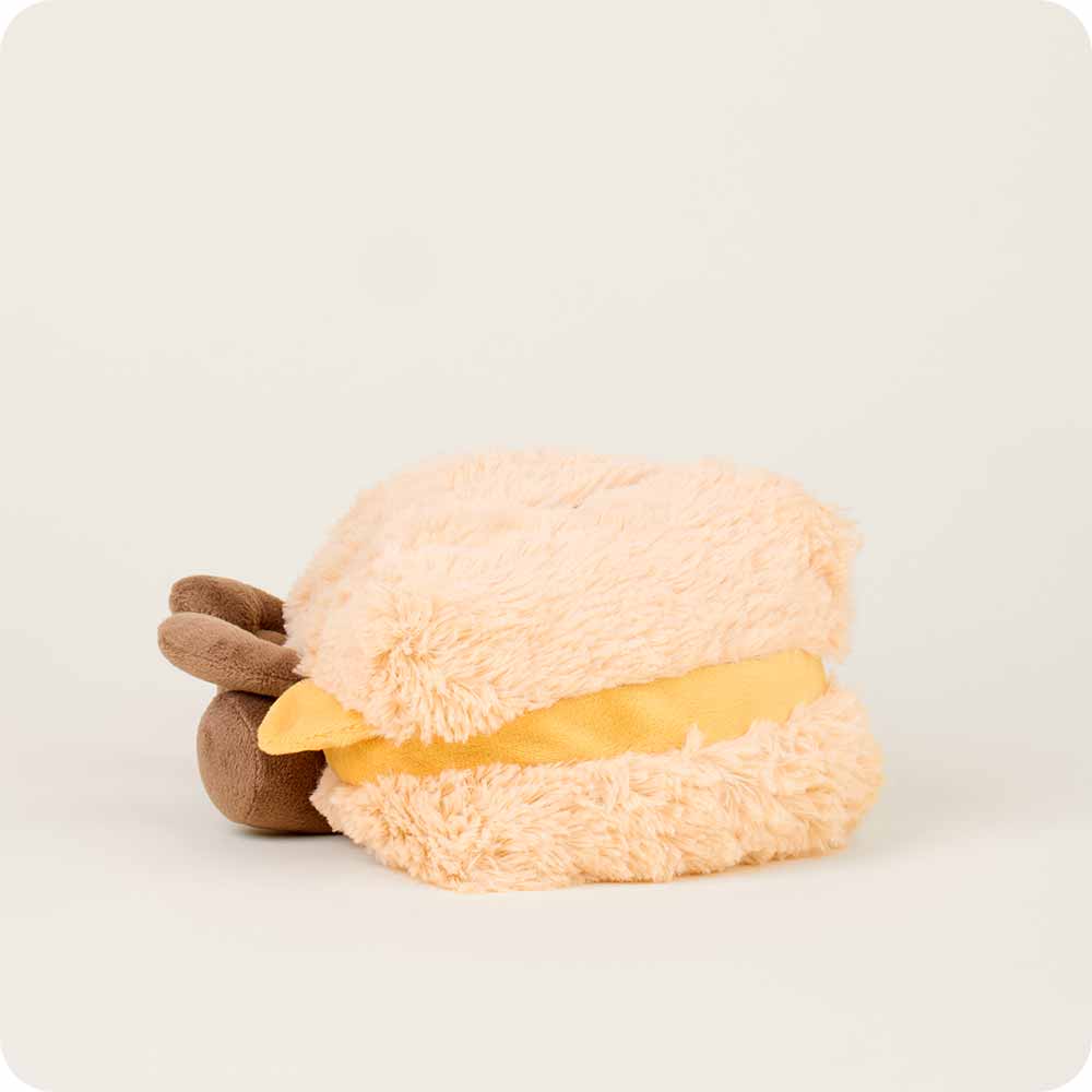 The Faire Grilled Cheese Warmies, a plush beige and yellow microwavable sensory toy with soft brown ends, sits on a plain off-white background.