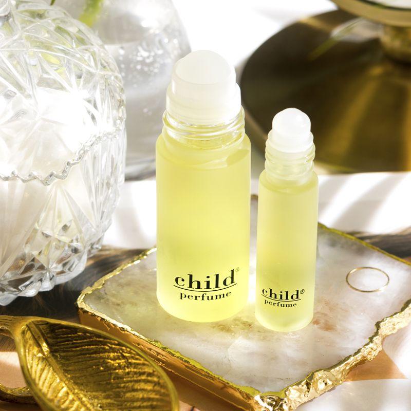 Two bottles of Faire Child Perfume Oil Roll sit on a marble tray, with a crystal jar and gold leaf accessory nearby, all bathed in bright natural light.