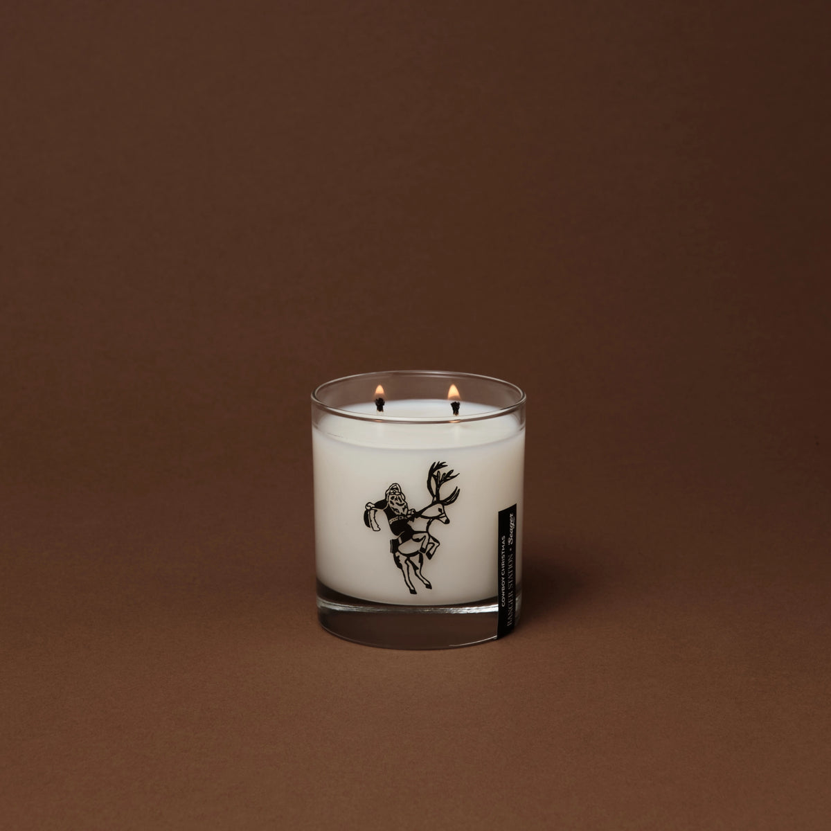 Cowboy Christmas candle in a glass jar featuring a black illustration of a cowboy riding a reindeer.