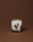 Cowboy Christmas candle in a glass jar featuring a black illustration of a cowboy riding a reindeer.