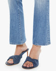 A person wearing The Outside Flood vintage blue jeans by Mother and dark blue heeled sandals with a knotted design stands on a white background.