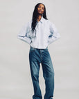 Blue striped cropped oxford shirt with loose blue jeans and white sneakers, styled by Denimist on a plain background.