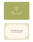 Rupi Kaur's Writing Prompts Gratitude by Simon & Schuster Inc. includes an olive green card with a white flower drawing and a cream card asking, "What changes in your life are you most grateful for?"—ideal for gratitude journaling.