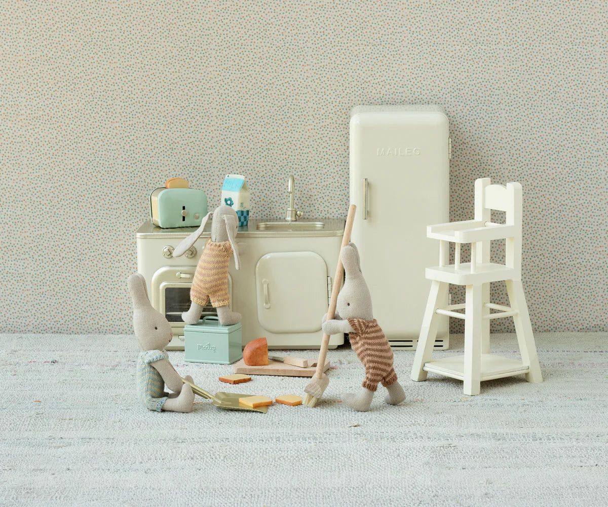 Three small Maileg plush bunnies play in a vintage-style kitchen, featuring the Maileg Bread box w. utensils, fridge, stove, sink, highchair, and dollhouse touches; two bunnies mop while another stands by the sink.