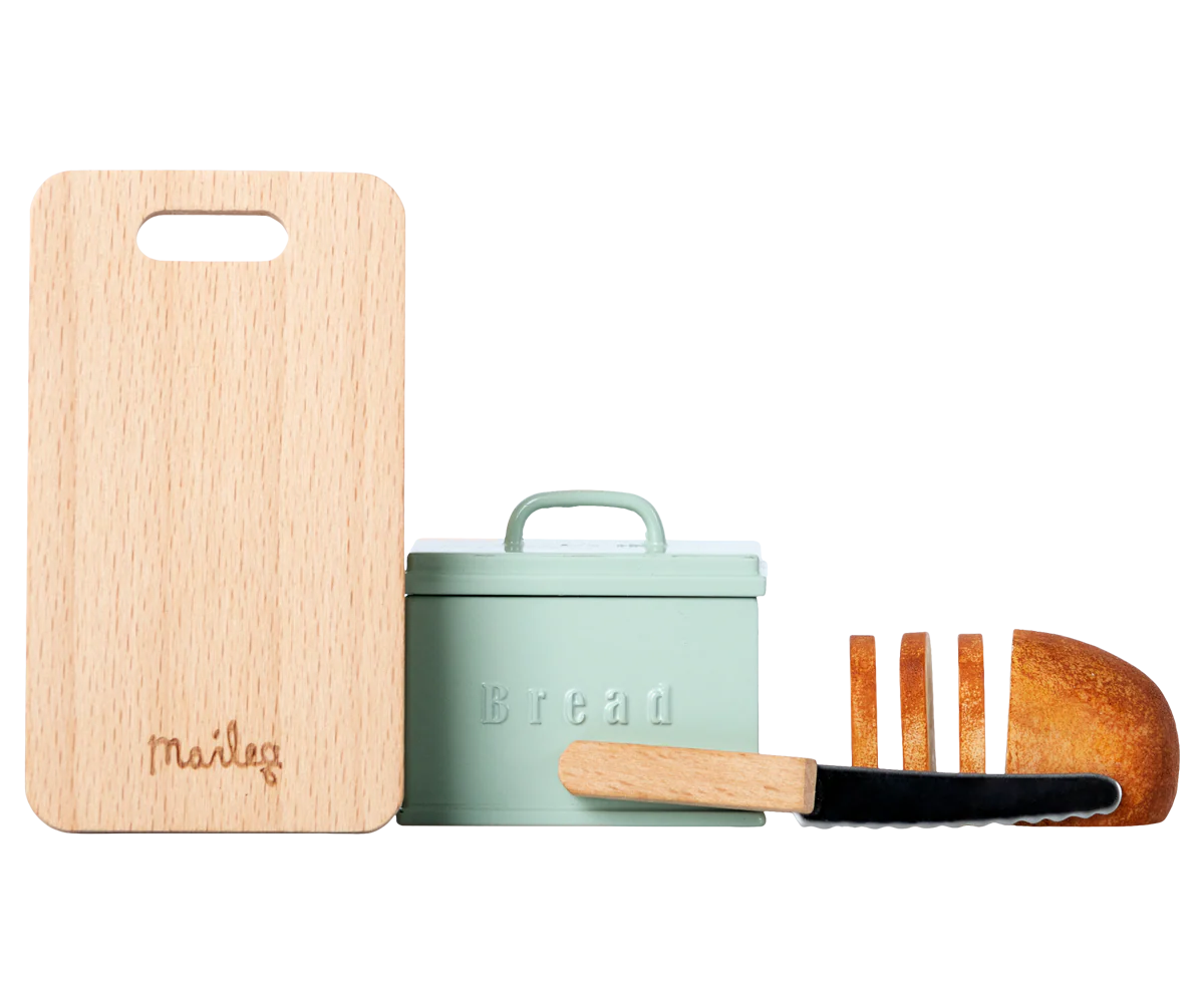 The Maileg Bread box w. utensils set by Maileg includes a mint green bread box labeled "Bread," a small wooden cutting board, a toy bread knife, and a sliced toy loaf—ideal accessories for any Maileg dollhouse.