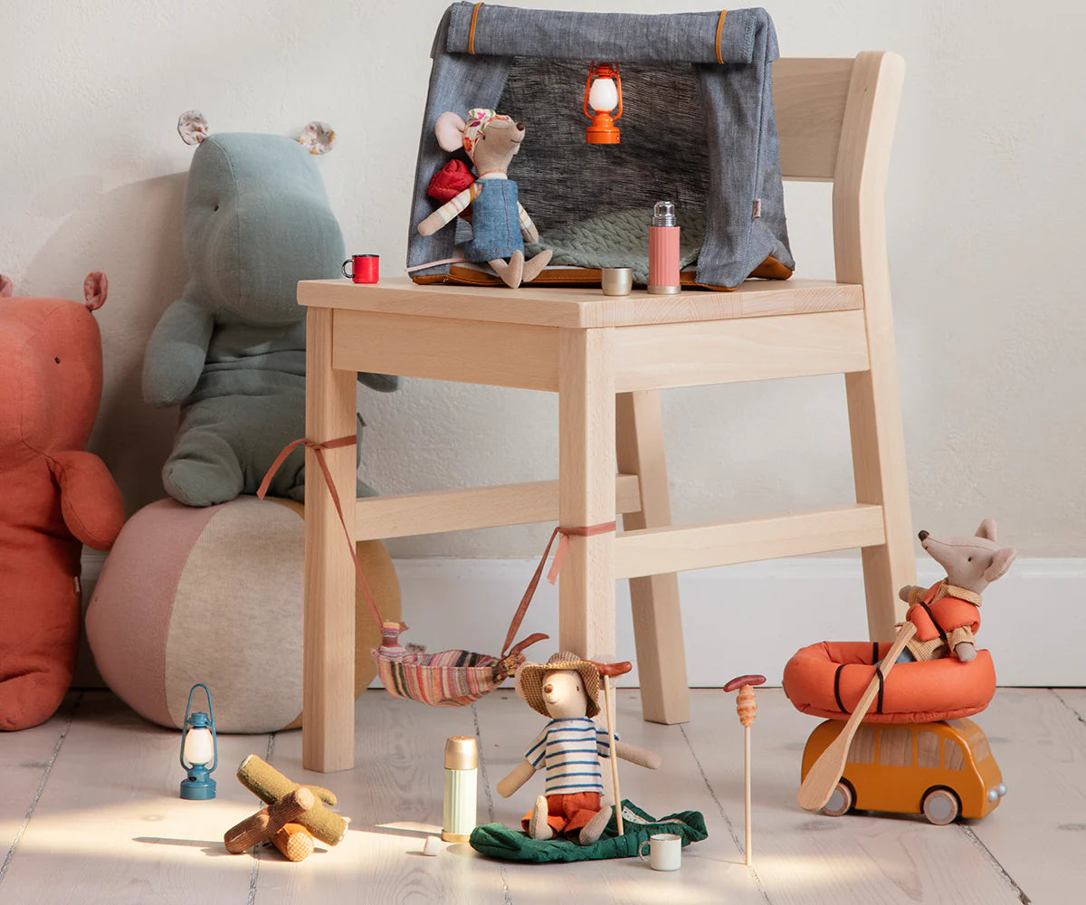 Maileg hiker mice with magnetic hands relax by a chair with camping gear, lanterns, and Thermos set; cozy adventure scene.