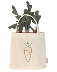 The Maileg Carrots in Bag by Maileg is a small beige tote with an embroidered carrot design and green leaves, perfect for imaginative play or as a cute decorative accent. It looks like fabric carrots are peeking out of the bag.