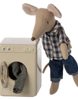 A Maileg mouse doll, dressed in a plaid shirt and jeans, stands next to the Maileg Washing Machine with checkered laundry partially inside.
