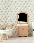 Two Maileg toy mice sit in a white bathtub in a dollhouse bathroom with a vanity, mirror, and the Maileg Toilet by Maileg. Light floral wallpaper and tiled flooring enhance the cozy, whimsical scene.