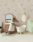 A Maileg Sink Dresser stands in a miniature bathroom scene with a toy mouse in a dress, white bathtub, toilet, mirror, and laundry on a clothesline against charming floral wallpaper.
