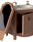 The Maileg Sink Dresser is a small brown toy vanity featuring a white bathroom sink, gold faucet, side mirror on the left, ramp at the base, and an open cabinet door—ideal as dollhouse furniture.
