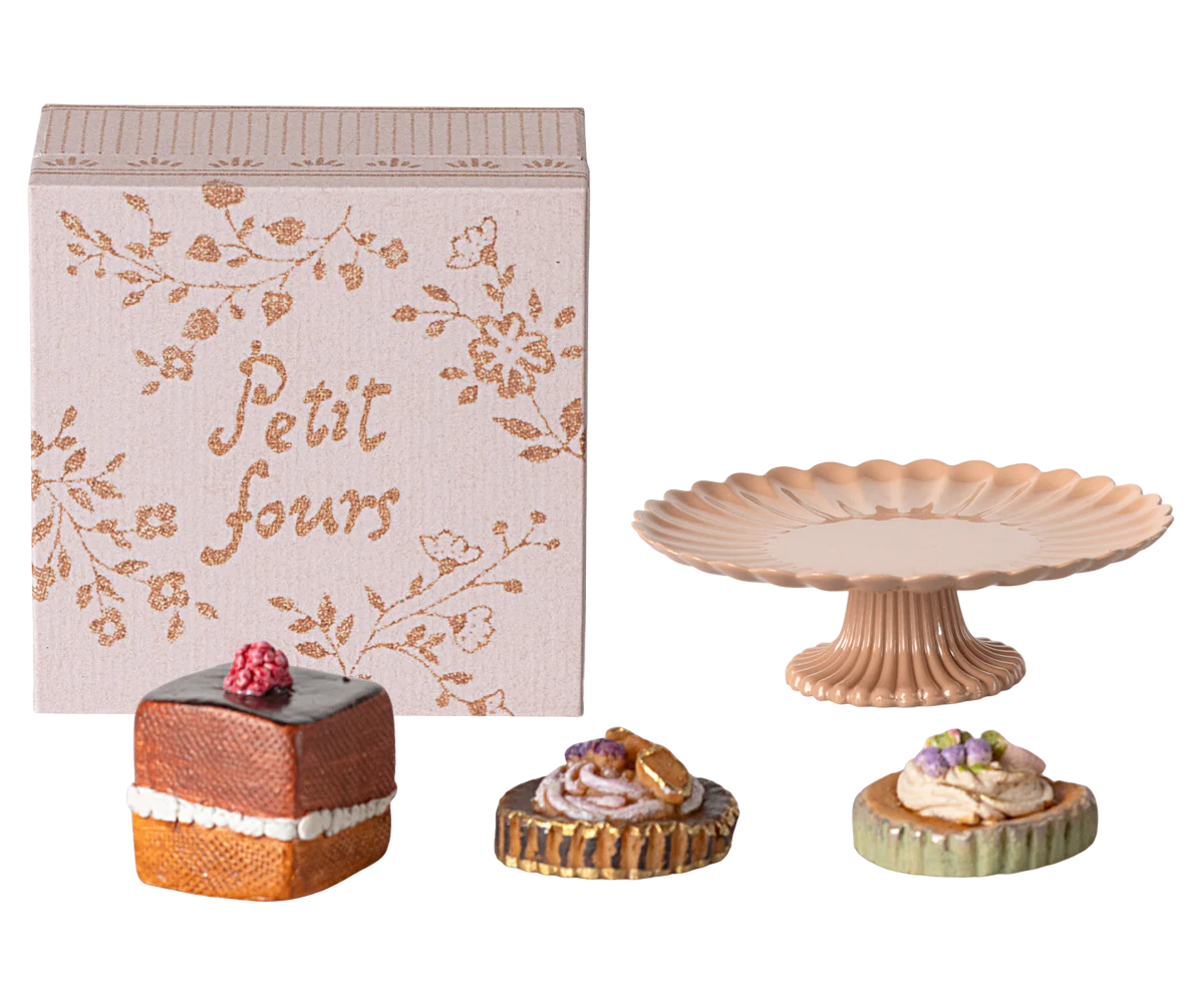The Maileg Cakes Display by Maileg features a decorative “Petit fours” box, a pink scalloped cake stand, and three dollhouse pastries artfully arranged on a white background.