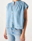 Someone wearing the AMO Denim Tessa Top, a light blue sleeveless button-up denim shirt with a high collar, paired with relaxed fit light blue jeans, made in Los Angeles, stands against a plain background.