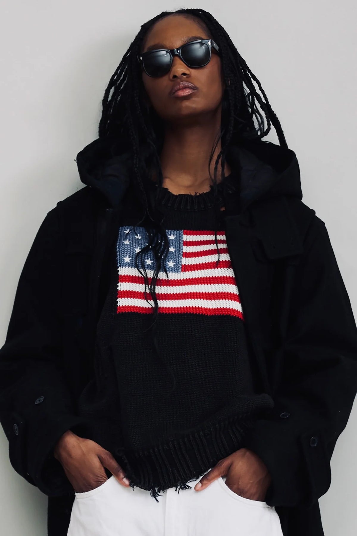 Distressed American flag sweater by Denimist worn under a black hooded jacket.