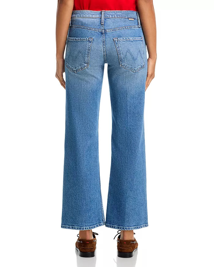 A person, seen from the back against a white background, wears Mother’s Lil Bookie Twist Skimp jeans in light blue with a five-pocket, high-waisted, wide-leg design and brown shoes.