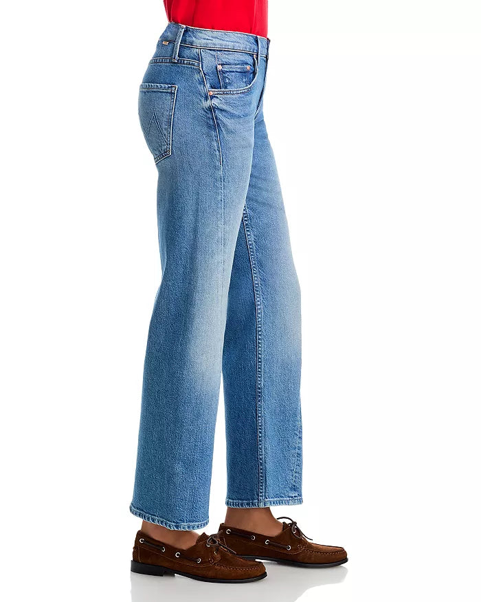 A person models the Mother Lil Bookie Twist Skimp light blue straight-leg jeans, styled with a red top and brown boat shoes, standing sideways against a white background.