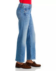 A person models the Mother Lil Bookie Twist Skimp light blue straight-leg jeans, styled with a red top and brown boat shoes, standing sideways against a white background.