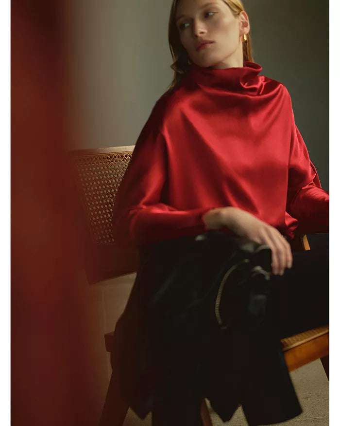Ilaria Draped Top in hammered satin worn by a woman seated on a wooden chair.