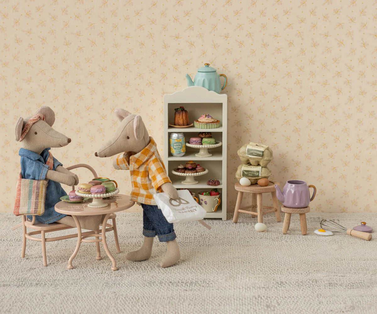 Two Maileg toy mice, including the Maileg Dad Mouse by Maileg, are in a miniature kitchen: Dad sits at a small table with pastries while the other holds a paper bag. Behind them is a shelf with desserts, kitchen items, and cute mouse accessories.