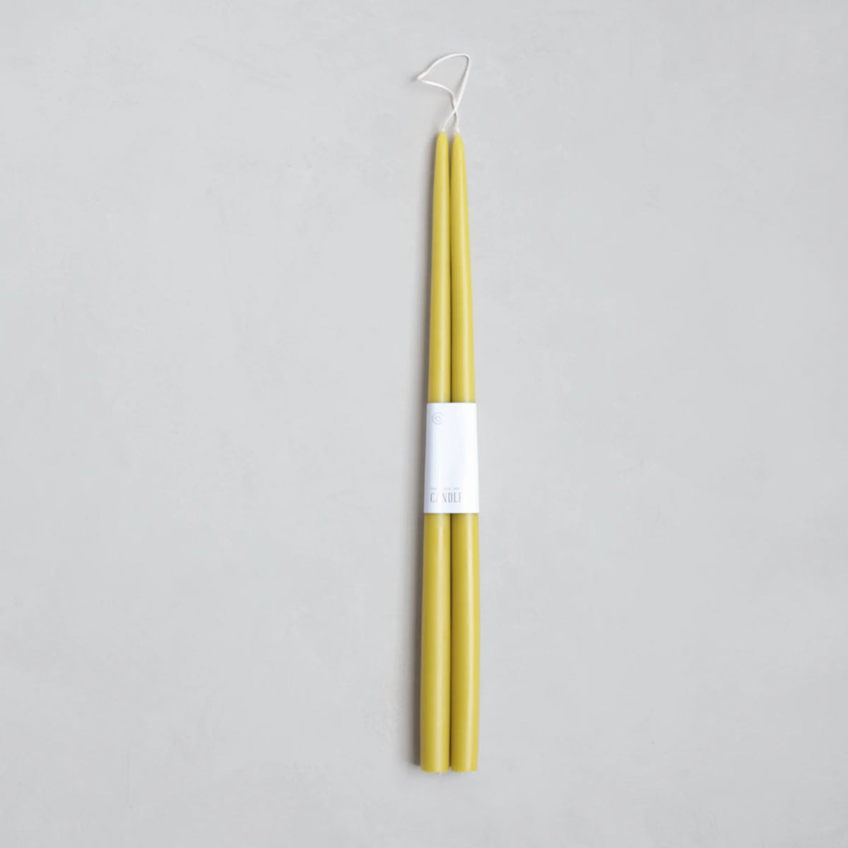 A pair of 18" Taper Candles by The Floral Society in yellow, crafted from premium materials, are joined at the wicks with a white label and displayed on a light gray background.