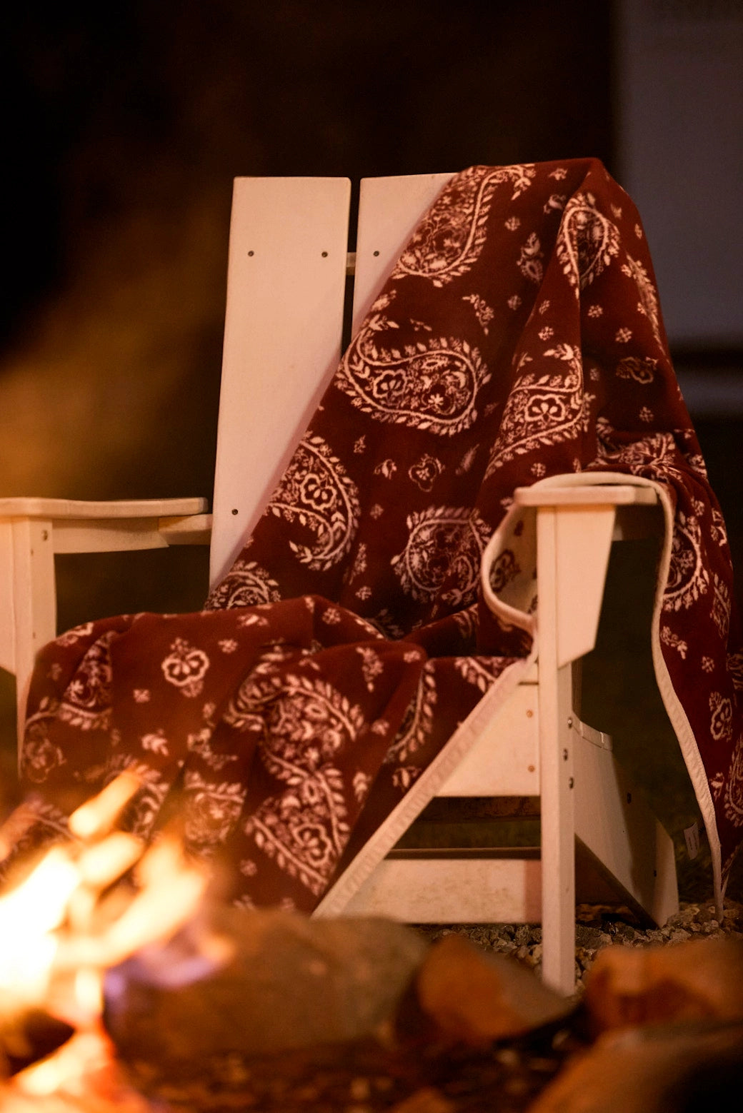 Faire Palmer Paisley Blanket draped on a white chair by an outdoor fire pit at night, cozy patio setting.