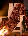 Faire Palmer Paisley Blanket draped on a white chair by an outdoor fire pit at night, cozy patio setting.