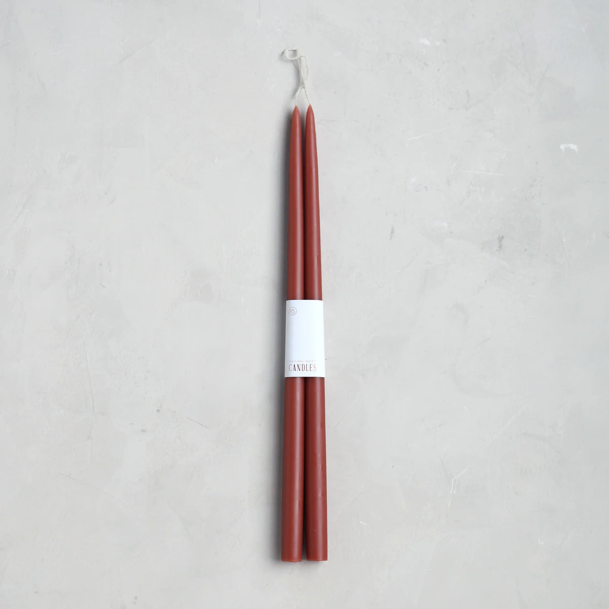A pair of 18" taper candles by The Floral Society, bundled with a white paper label, are shown on a light gray textured surface.