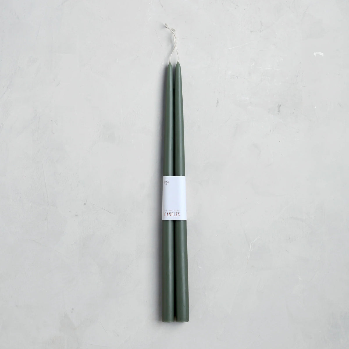 A pair of 18" Taper Candles by The Floral Society, featuring an elegant dark green design with white labels, set against a light gray textured background.