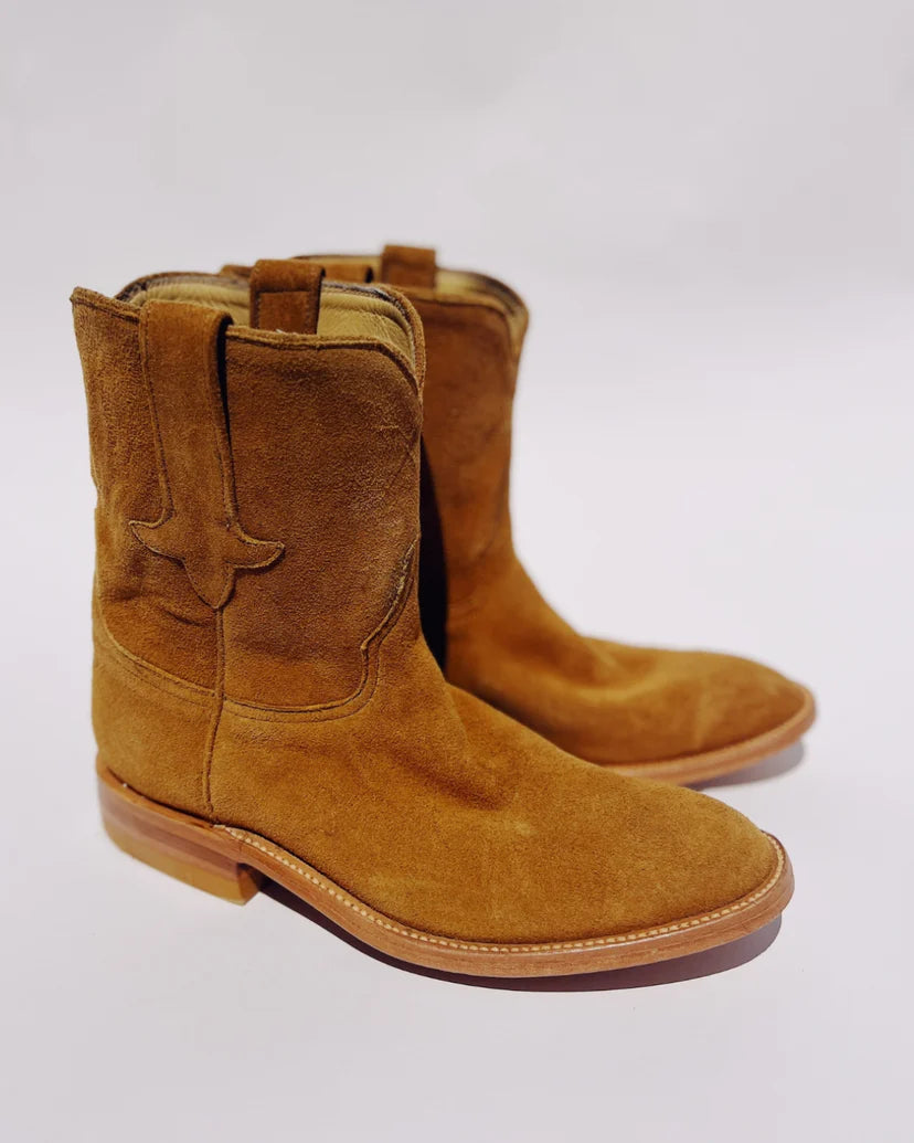 Hey Gang's The Ranch Boot showcases brown calfskin suede with decorative side stitching, a light wooden sole, and stacked heel. Placed on a plain white background, they exude timeless western charm.