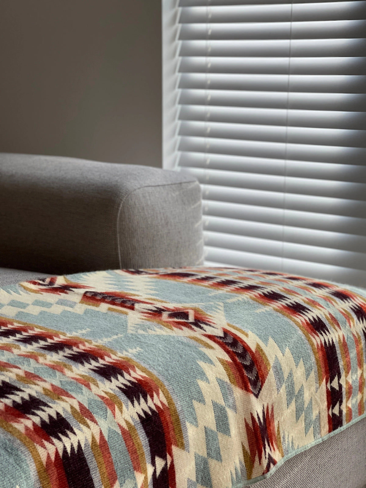 Secoya Throw in vibrant mint with a geometric southwestern pattern, draped over a gray sofa from Bungalow Furniture.