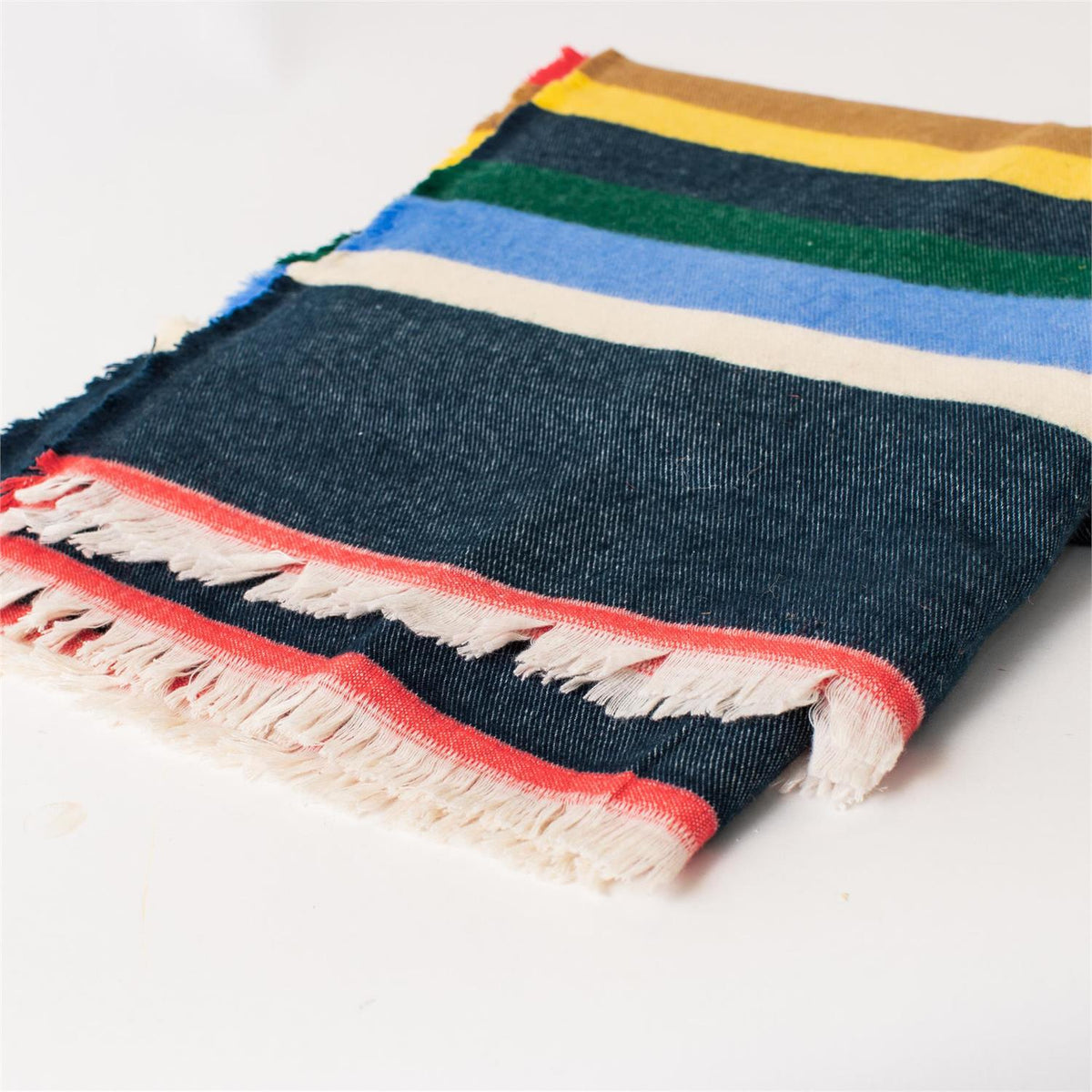 The Faire Multicolor Cabin Stripe Throw Blanket features horizontal yellow, green, blue, cream, and red stripes on a dark denim background with white fringe—ideal for rustic home decor or as a cozy cabin throw.