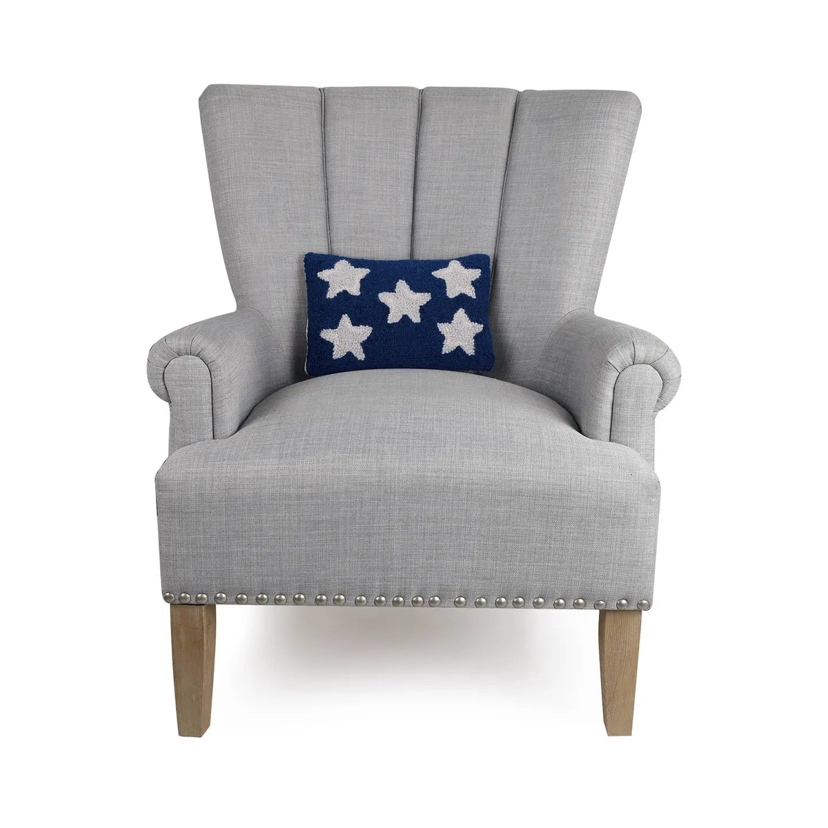A light gray upholstered armchair with wooden legs and silver nailhead trim features Faire’s Patriotic Stars Pillow, a navy wool hooked throw pillow with five white stars—an ideal subtle 4th of July accent.