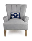 A light gray upholstered armchair with wooden legs and silver nailhead trim features Faire’s Patriotic Stars Pillow, a navy wool hooked throw pillow with five white stars—an ideal subtle 4th of July accent.