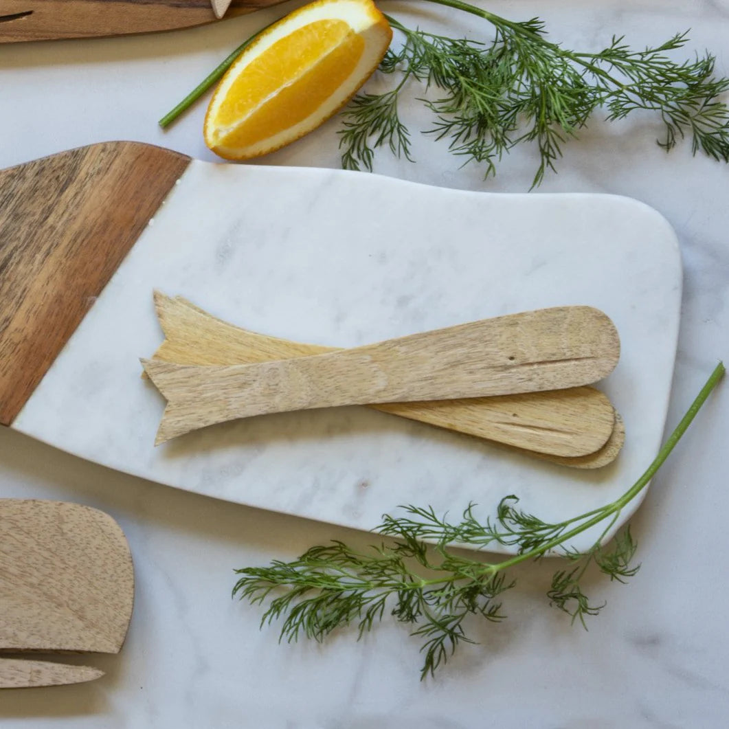 Set of four mango wood whale-shaped spreaders by Be Home on marble, styled with dill and an orange wedge.