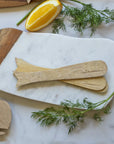 Set of four mango wood whale-shaped spreaders by Be Home on marble, styled with dill and an orange wedge.