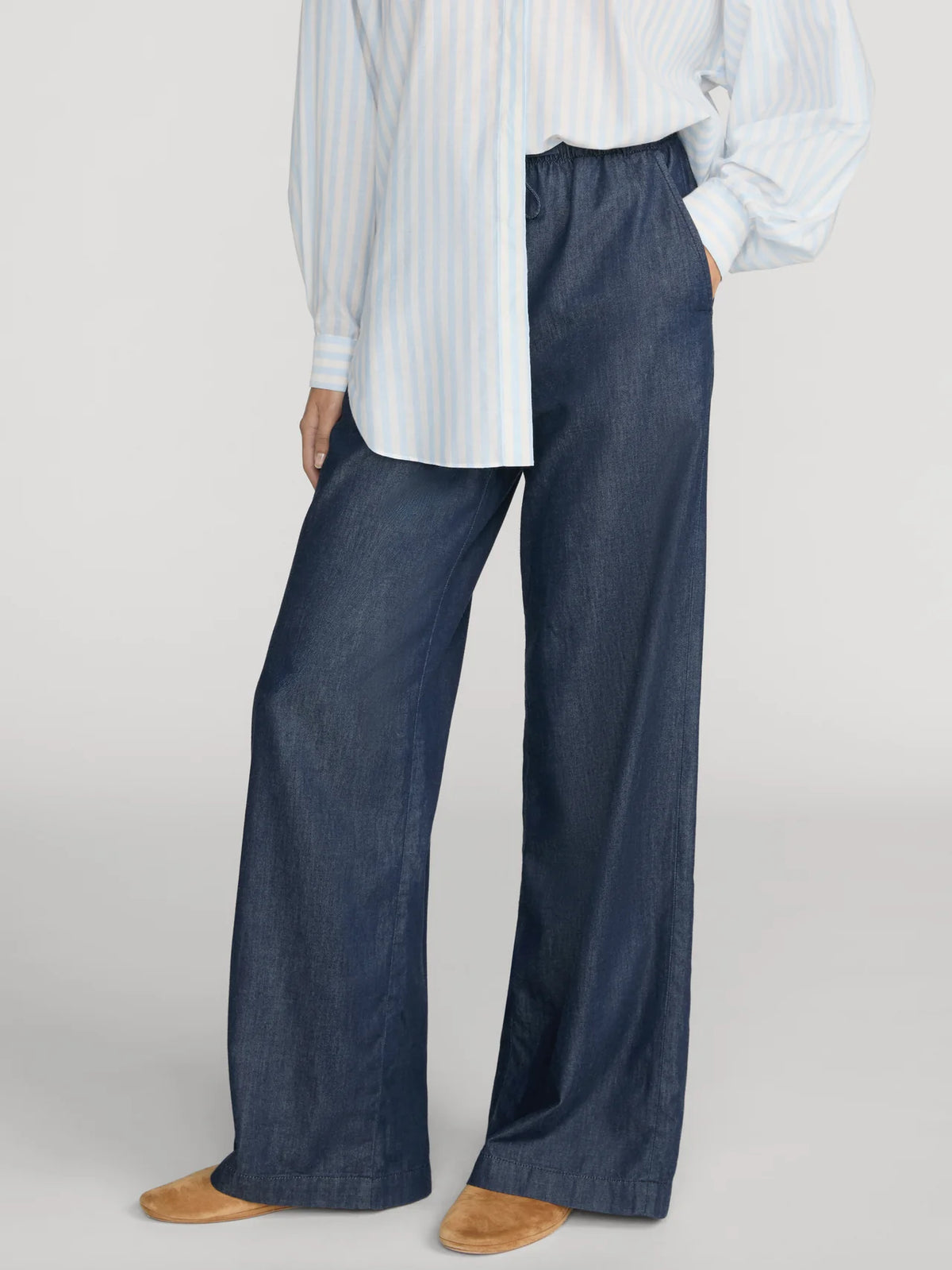 Relaxed dark blue FRAME Offshore Pant styled with striped shirt and tan shoes, set against a neutral gray backdrop.
