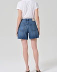 A person stands facing away against a plain light background, wearing a white t-shirt, heeled sandals, a gold chain necklace, and the Citizens Of Humanity/AGOLDE brynn drawstring short in avant (lightwt vintage).