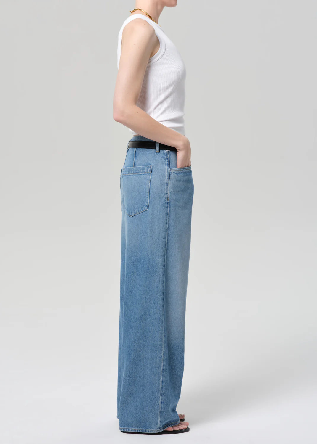 A person in Citizens Of Humanity/AGOLDE's velha trouser in soiree, light blue relaxed non-stretch denim jeans, stands in profile with one hand in their pocket against a plain light gray background.