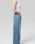 A person in Citizens Of Humanity/AGOLDE's velha trouser in soiree, light blue relaxed non-stretch denim jeans, stands in profile with one hand in their pocket against a plain light gray background.