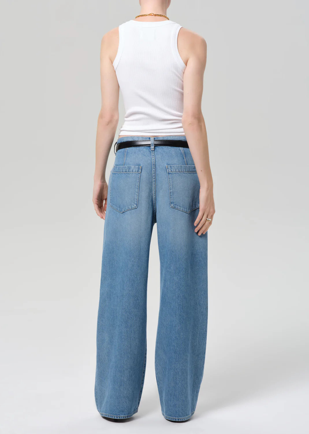 A person faces away against a plain background, wearing a white sleeveless ribbed tank and Citizens Of Humanity/AGOLDE velha trouser in soiree—high-waisted, relaxed blue jeans with large back pockets, non-stretch denim, and recycled cotton.