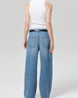 A person faces away against a plain background, wearing a white sleeveless ribbed tank and Citizens Of Humanity/AGOLDE velha trouser in soiree—high-waisted, relaxed blue jeans with large back pockets, non-stretch denim, and recycled cotton.