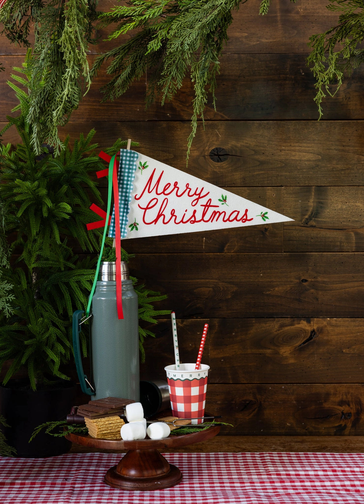 Merry Christmas felt pennant flag on a wooden stand with red ribbons and s’mores ingredients by Bungalow.