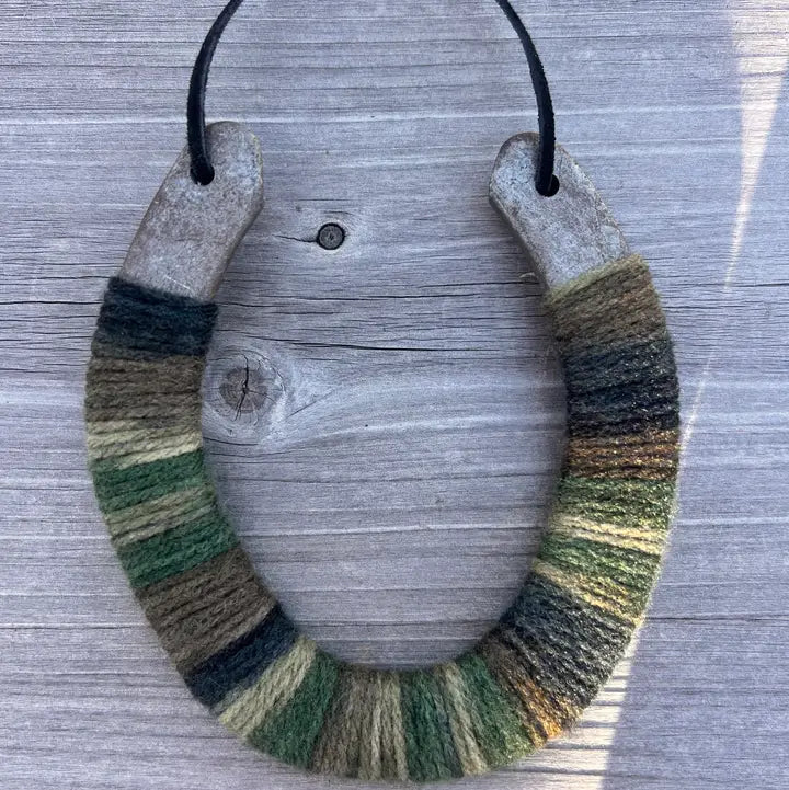 The Lucky Horseshoe by Faire features a bottom half wrapped in multicolored green and brown yarn, hanging on light wood—a rustic upcycled décor piece or unique personalized gift.