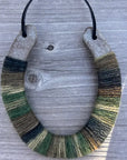 The Lucky Horseshoe by Faire features a bottom half wrapped in multicolored green and brown yarn, hanging on light wood—a rustic upcycled décor piece or unique personalized gift.