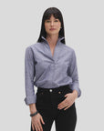 A woman with straight black hair models the Denim Country Club shirt by Sarah Alexandra, LLC. She pops the flared collar and pairs it with black jeans and a bracelet, standing against a plain light gray background.