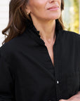A woman models the Frank & Eileen Mary Classic Shirtdress - Ruffle outdoors, smiling softly with her upper body and part of her face visible as she stands slightly turned to the side.