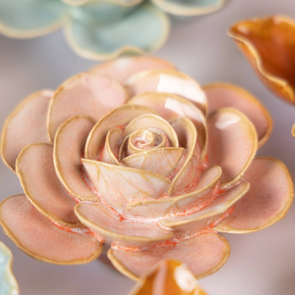 Close-up of Faire's Peach Pink Cloni Ranunculus, featuring ceramic flowers with pink and peach-toned petals, a glossy finish, and intricate detailing, set against a blurred pastel background.